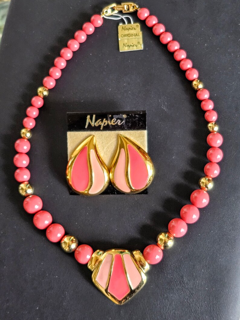 Pu&ograve; includere: Un set di collana e orecchini rosa e oro con un design geometrico. La collana &egrave; realizzata con perline rosa con accenti dorati e un grande ciondolo geometrico. Anche gli orecchini sono geometrici e presentano accenti rosa e oro. Il set &egrave; etichettato "Napier Original".