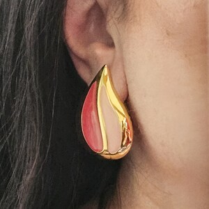 Pu&ograve; includere: Orecchini a goccia dorati con smalto rosa e rosso.