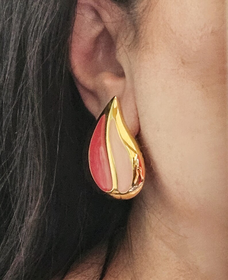 Pu&ograve; includere: Orecchini a goccia dorati con smalto rosa e rosso.