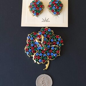 Pode incluir: Um conjunto de joias vintage de Albert Weiss. O conjunto inclui um broche e um par de brincos. O broche tem a forma de uma flor com pedras de imita&ccedil;&atilde;o vermelhas, azuis e verdes. Os brincos t&ecirc;m a forma de um cora&ccedil;&atilde;o e tamb&eacute;m apresentam pedras de imita&ccedil;&atilde;o vermelhas, azuis e verdes.