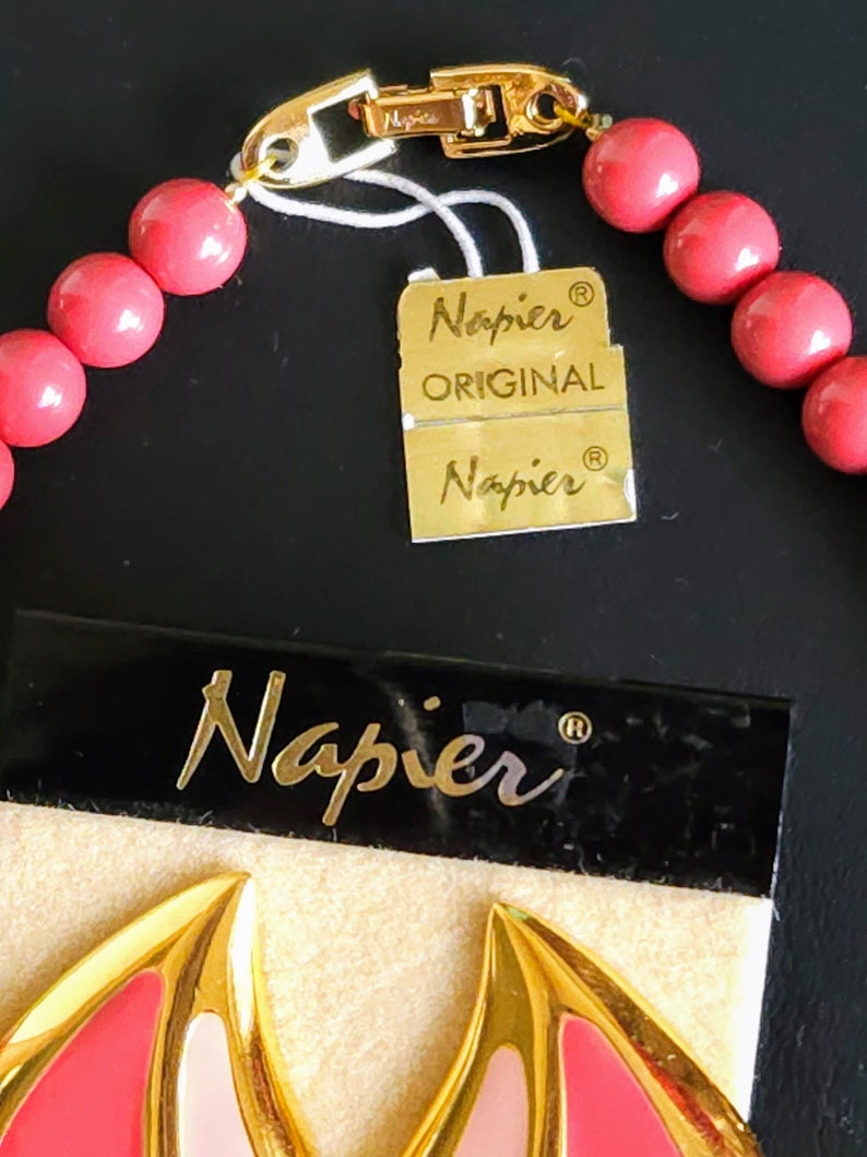 Pu&ograve; includere: Una collana rosa e oro con una chiusura dorata e un'etichetta che recita "Napier Original Napier".