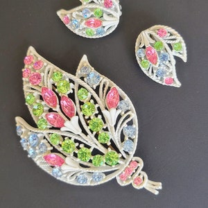 Pu&ograve; includere: Un set vintage di spilla e orecchini con un design floreale con strass rosa, verdi e blu. Il set &egrave; realizzato in metallo bianco e presenta un design delicato e intricato.