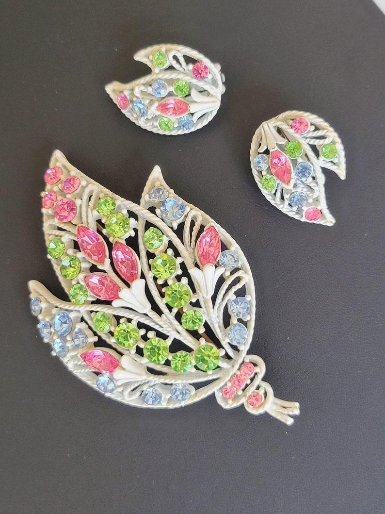 Pu&ograve; includere: Un set vintage di spilla e orecchini con un design floreale con strass rosa, verdi e blu. Il set &egrave; realizzato in metallo bianco e presenta un design delicato e intricato.
