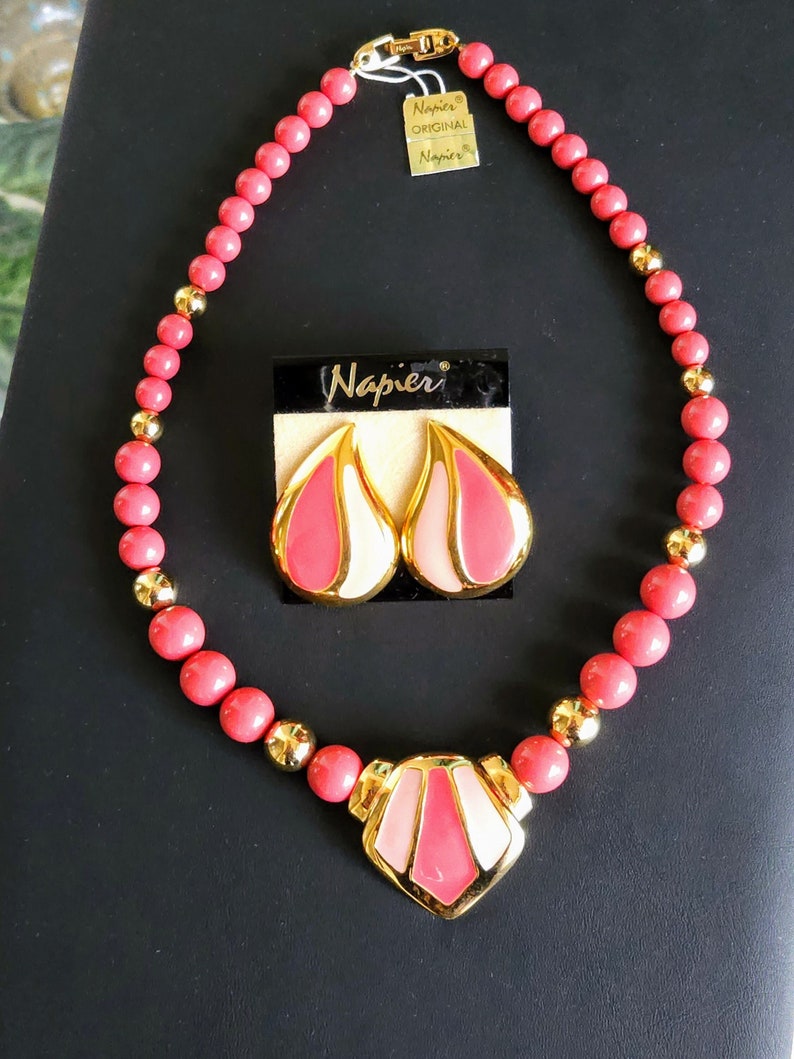 Pu&ograve; includere: Una collana rosa e oro con un ciondolo geometrico e orecchini abbinati. La collana &egrave; realizzata con perline rosa e dettagli dorati. Anche gli orecchini sono rosa e oro con un design geometrico. L'etichetta sulla collana recita "Napier Original Napier".