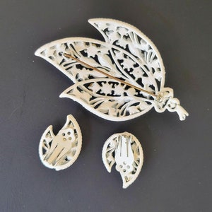 Pu&ograve; includere: Un set di spilla e orecchini in filigrana bianca con un design floreale. La spilla ha un fermaglio a spilla e gli orecchini hanno fermagli a clip.