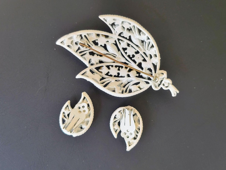 Pu&ograve; includere: Un set di spilla e orecchini in filigrana bianca con un design floreale. La spilla ha un fermaglio a spilla e gli orecchini hanno fermagli a clip.