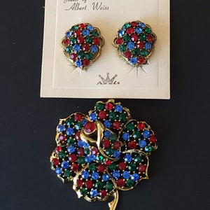 Pode incluir: Um conjunto de joias vintage da Albert Weiss, incluindo um broche e brincos. O broche &eacute; uma flor dourada com pedras de strass vermelhas, azuis e verdes. Os brincos s&atilde;o cachos correspondentes de pedras de strass vermelhas, azuis e verdes.