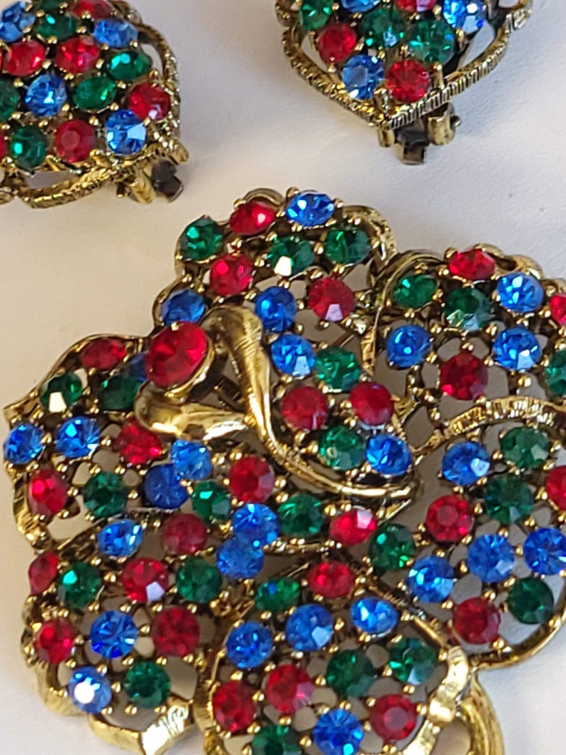 Pode incluir: Um par de brincos em tom dourado com um design de borboleta. As borboletas s&atilde;o cobertas com strass vermelhos, azuis e verdes.