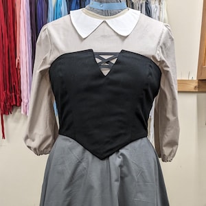 Puede incluir: Un vestido gris, blanco y negro con un corpiño ajustado y una falda completa. El corpiño tiene un detalle de encaje negro y un cuello blanco.