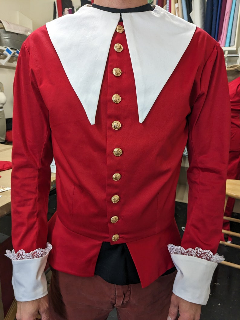 May include: A red long-sleeved shirt with a white collar and gold buttons. The shirt has a pointed collar and lace trim on the cuffs.