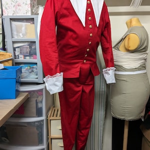 May include: A red and white costume with a large white collar and gold buttons. The costume includes a jacket and pants.