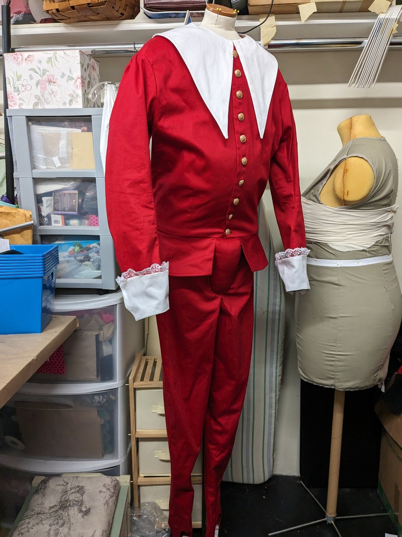 May include: A red and white costume with a large white collar and gold buttons. The costume includes a jacket and pants.