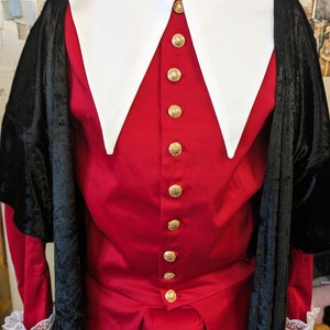 May include: A red and black costume with a large white collar and gold buttons. The costume is made of velvet and has a long, flowing cape.
