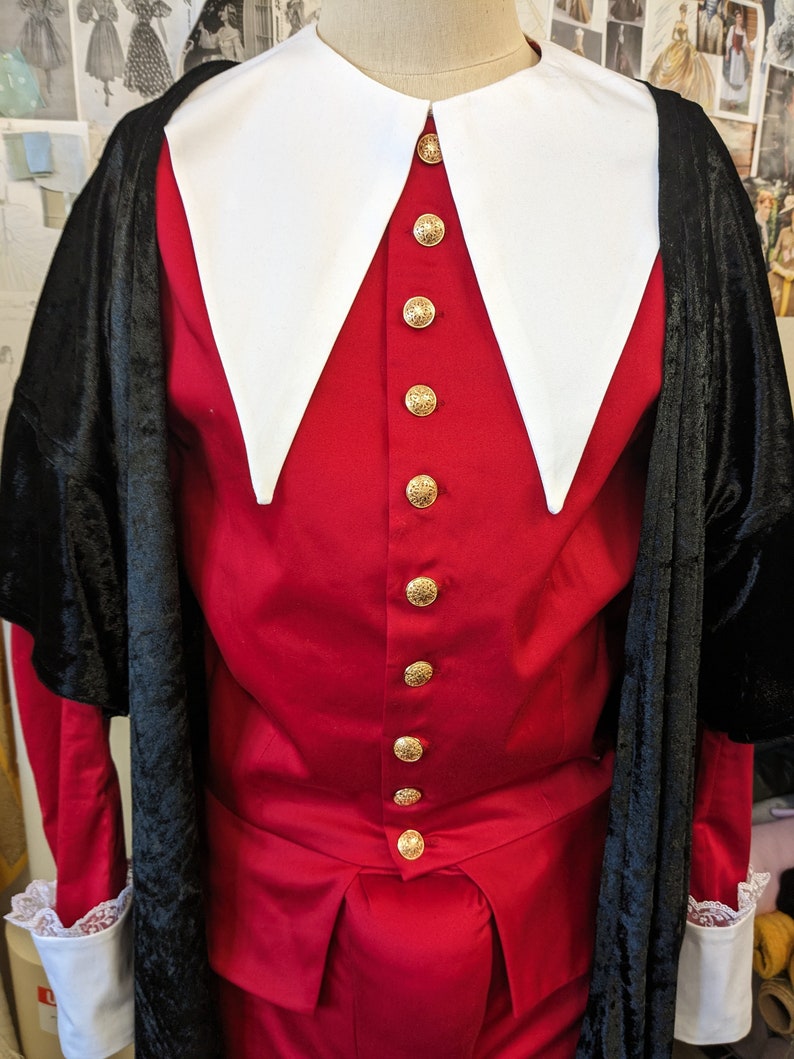 May include: A red and black costume with a large white collar and gold buttons. The costume is made of velvet and has a long, flowing cape.
