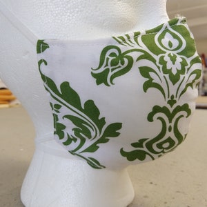 May include: White face mask with a green damask pattern. The mask is made of fabric and has a white background with green floral designs.