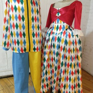 May include: A red and white harlequin costume with a diamond pattern. The costume includes a jacket, pants, and a skirt. The jacket has a yellow zipper and a green stripe down the front. The pants are blue and yellow. The skirt is red, white, blue, green, and yellow.