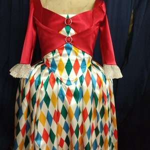 May include: A red and white dress with a diamond pattern. The dress has a red bodice with a white collar and long sleeves. The skirt is white with red, yellow, blue, and green diamond shapes.