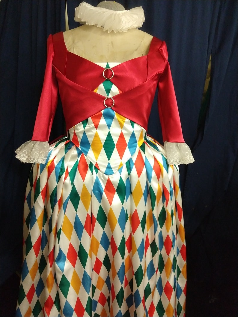 May include: A red and white dress with a diamond pattern. The dress has a red bodice with a white collar and long sleeves. The skirt is white with red, yellow, blue, and green diamond shapes.