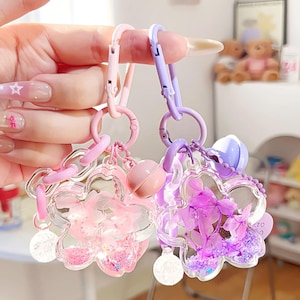 May include: Two flower-shaped keychains with clear acrylic petals, filled with pink and purple accents. Each keychain has a different color scheme, one pink and the other purple, with matching hardware and a small charm.