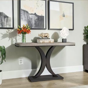 May include: A console table with a rectangular grey wood-grain top and a dark brown base featuring two curved legs. On the table sits a clear glass vase with orange flowers, a gold-toned rhinoceros figurine, and a white abstract sculpture.