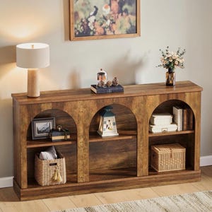 May include: A wooden console table with three arched sections, each with a shelf. The table is adorned with decorative items such as a lamp, framed art, a lantern, books, and a basket. The table has a warm, brown finish.