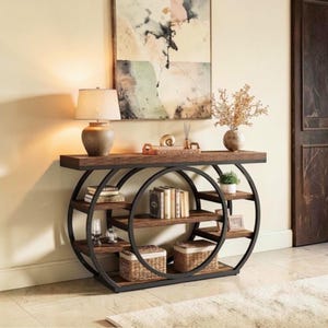 May include: A rectangular console table featuring a dark brown wooden top and shelves supported by two large black metal circular frames. The unit includes multiple storage levels holding books, two woven baskets, and decorative glass items.