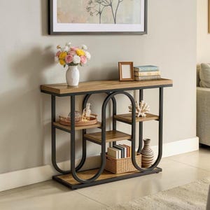 May include: A console table featuring a rectangular wooden top and base with black metal U-shaped supports. The unit includes two tiered shelves, a woven basket, a white vase with flowers, a small picture frame, and stacked books.