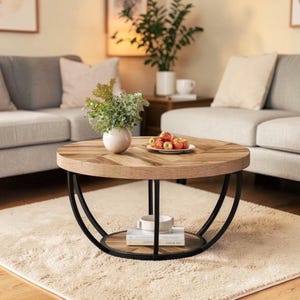 May include: A circular coffee table with a wooden herringbone top and a black metal frame. The table features a lower shelf and is set on a beige rug, with two grey sofas in the background. A vase of flowers and a plate of apples are on the table.
