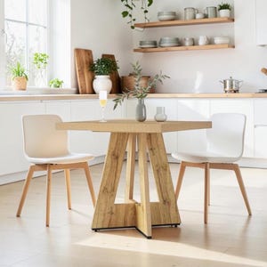 May include: A square wooden dining table with a light oak finish and a central pedestal base, accompanied by two white chairs with light wooden legs. The table surface holds a clear glass of liquid and a grey vase containing a green leafy branch.
