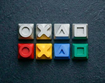 May include: Eight colorful square buttons with iconic gaming symbols: circle, X, triangle, square. The buttons are in red, yellow, blue, and green, with a dark background. A gaming-themed design.