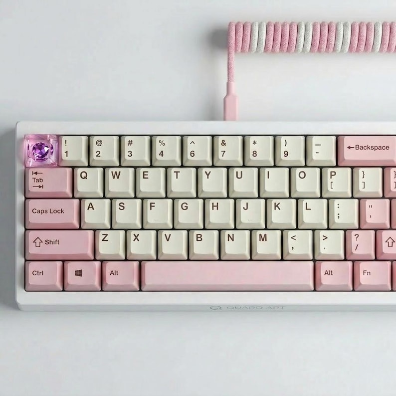 May include: A white mechanical keyboard with pink and cream-colored keycaps. The keyboard has a coiled cable with pink and white stripes. The keycaps are arranged in a standard QWERTY layout, with a few custom keycaps.