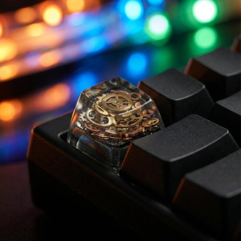 May include: Close-up of a custom keyboard keycap with a steampunk design. The keycap is clear with embedded brass gears and mechanical components. The keycap is installed on a black keyboard.