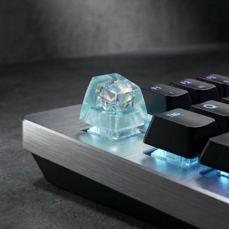 May include: Close-up of a mechanical keyboard with a custom keycap. The keycap is a clear, light blue design encasing a multi-faceted, diamond-shaped crystal. The keyboard has a brushed metal finish and black keys.
