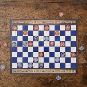 May include: A board game with a blue, white, and marble design, featuring red and yellow circular game pieces. The board has a Greek key border and is set on a wooden surface. Several game pieces are scattered around the board.