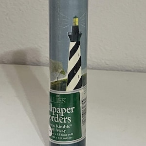 Pode incluir: Um rolo cilíndrico de borda de papel de parede com um farol de listras diagonais pretas e brancas. O rótulo exibe o texto 'ALLIES wallpaper borders Warren Kimble Sail Away 4,5 metros'. O design inclui uma luz amarela.