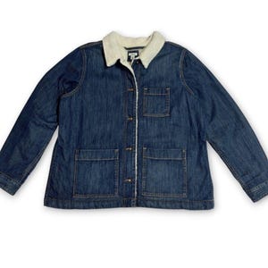 May include: A dark blue denim jacket featuring a white sherpa collar and lining, a button-up front, one chest pocket, and two large lower front pockets. The jacket has long sleeves with buttoned cuffs and visible stitching throughout the fabric.