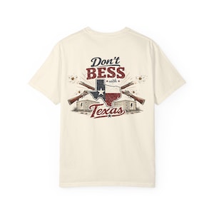 May include: Cream-colored t-shirt with a distressed graphic featuring the Texas state outline in red, white, and blue, crossed rifles, and the text "Don't Bess with Texas."