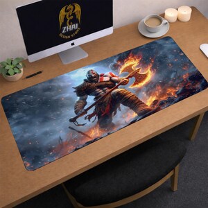 Peut inclure: Tapis de souris rectangulaire pour le jeu, avec une illustration détaillée d'un guerrier musclé avec un tatouage rouge, tenant une hache incandescente. Le fond montre des flammes et une atmosphère enfumée. Le tapis est sur un bureau en bois.