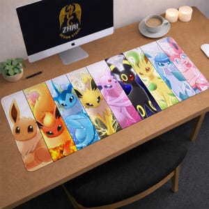 May include: A rectangular desk mat with a vibrant design of cartoon creatures. The mat is split into vertical sections, each displaying a different character in bright colours. The mat is on a wooden desk, with a computer monitor and other items visible in the background.