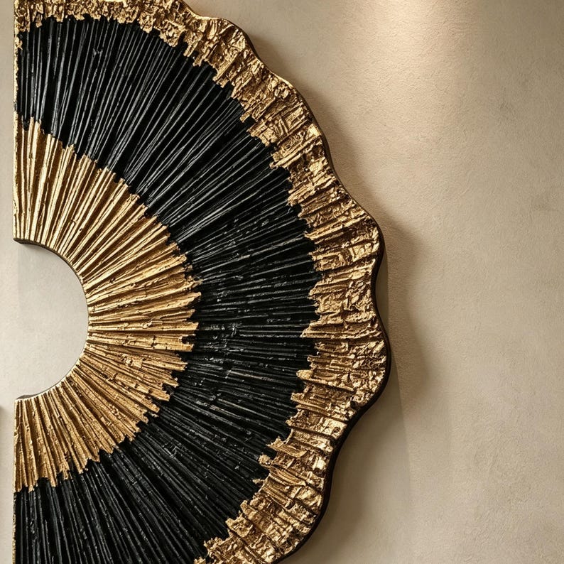 Op de afbeelding: Een halfrond wandkunstobject met een radiaal patroon van afwisselend zwarte en gouden getextureerde banden. Het ontwerp bestaat uit dunne, verhoogde lijnen die vanuit een centraal punt uitstralen, met een ruwe, metallic gouden rand.