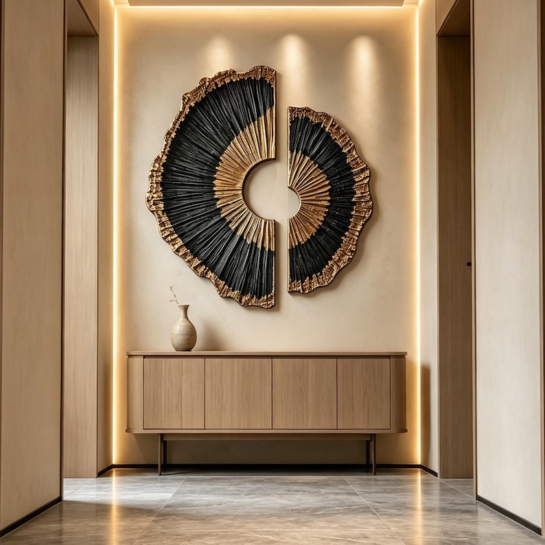 Op de afbeelding: Een tweedelige cirkelvormige wandsculptuur met een gestructureerd zwart en goudkleurig waaiervormig patroon, gemonteerd boven een lichthouten dressoir met vier deuren en een kleine keramische vaas aan de linkerkant.
