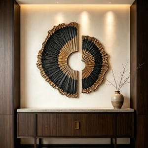 Op de afbeelding: Een tweedelige wandkunstset met cirkelvormige, waaiervormige figuren met gestructureerde zwarte en gouden stralende lijnen. De stukken zijn aan een muur bevestigd boven een donkerhouten dressoir met een kleine keramische vaas met takken.