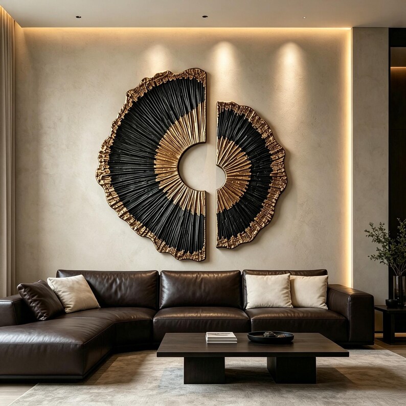 Op de afbeelding: Een grote, tweedelige cirkelvormige wanddecoratie met een gestructureerd, waaierachtig patroon in zwart en metallic goud. Het ontwerp bestaat uit twee asymmetrische helften met stralende lijnen die een zonnestraaleffect op de muur cre&euml;ren.