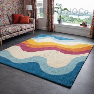 May include: A rectangular rug with a vibrant, wavy pattern. The rug showcases bands of blue, light blue, cream, yellow, orange, and magenta. It's placed on a dark grey floor in a room with a sofa and a window.
