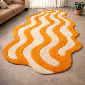 May include: A modern rug with an abstract design. The rug features a wavy pattern in orange and cream, creating a striking visual effect. The rug's irregular shape and bold colour scheme make it a statement piece for any living space. The rug is placed on a grey floor.