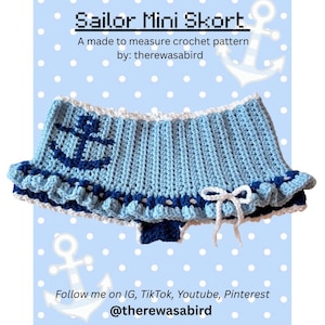 Pode incluir: Minissaia de crochê azul claro com tema marinheiro, com um desenho de âncora azul escuro e detalhes brancos. A saia tem uma bainha com babados e um laço branco. O texto "Sailor Mini Skort" está no topo.
