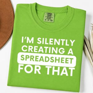 Peut inclure: Un t-shirt à manches courtes vert citron avec un col rond. Le t-shirt présente un texte blanc qui dit I'M SILENTLY CREATING A SPREADSHEET FOR THAT, avec le mot SPREADSHEET enfermé dans un élément graphique rectangulaire blanc aux coins arrondis.