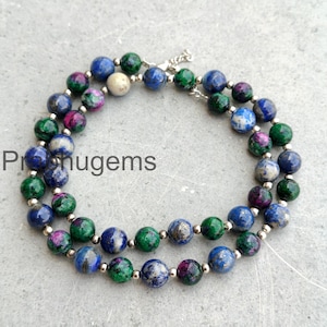 Puede incluir: Un collar de doble hebra con cuentas redondas en tonos azules, verdes, morados y blancos. Las cuentas están ensartadas en una cadena plateada. El texto "Pronugems" es visible en el lado izquierdo de la imagen.