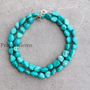 May include: A turquoise gemstone necklace with a silver clasp. The necklace is made of polished, irregular-shaped turquoise beads. The text "Prabhu Gems" is visible in the lower left corner.