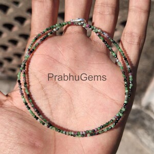 May include: A double-strand bracelet with small, round beads in green, black, and pink. The bracelet is fastened with a silver clasp. The text "PrabhuGems" is visible in the image.